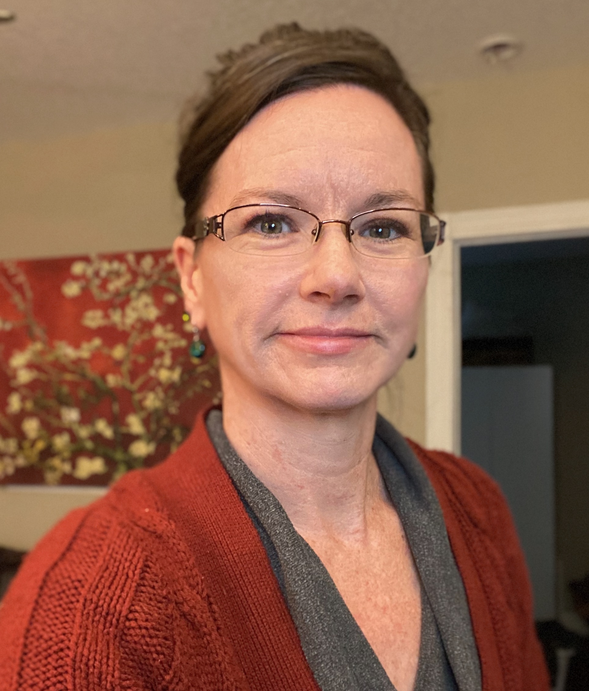 Headshot of barbara smiling and wearing a gray shirt with a red cardigan in a room in a home with a red photo on the wall in the background