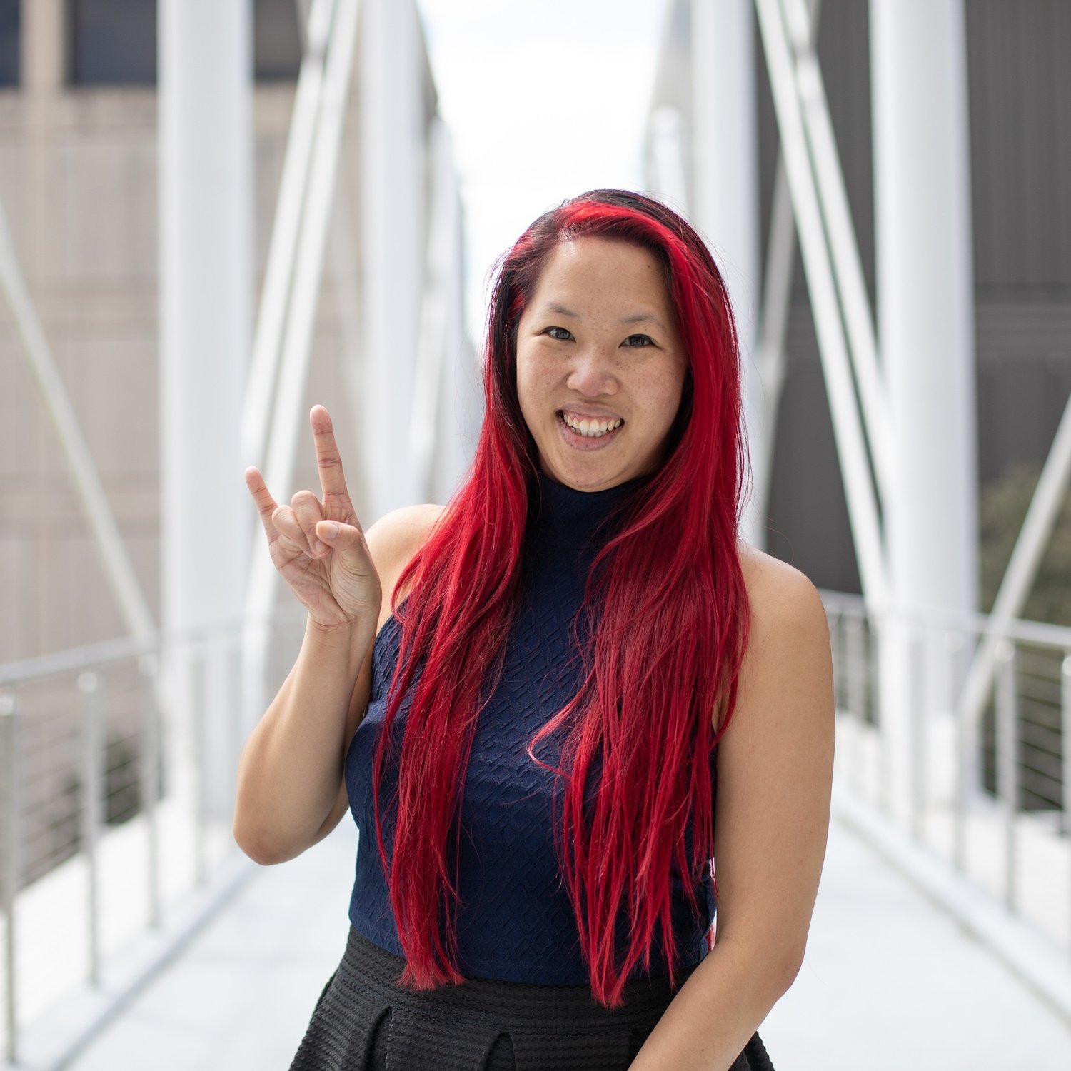 A photo of Jo from the torso up wearing a blue sleeveless turtle neck shirt with a white industrial background
